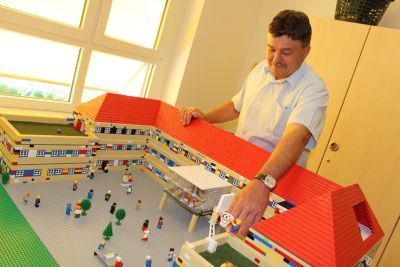 Schulleiter Frank Keck steht vor dem Modell des Schulgebäudes aus Legosteinen. Foto: Ministerium der Finanzen des Landes Sachsen-Anhalt