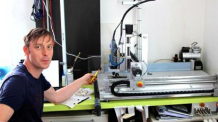 Das Foto zeigt den Geschäftsführer und Entwickler David Goll im blauen T-Shirt. Er sitzt an einem Tisch mit einer Fräsmaschine; mitten im Labor Labor der Firma Lagotec. (Foto: Friedemann Kahl)